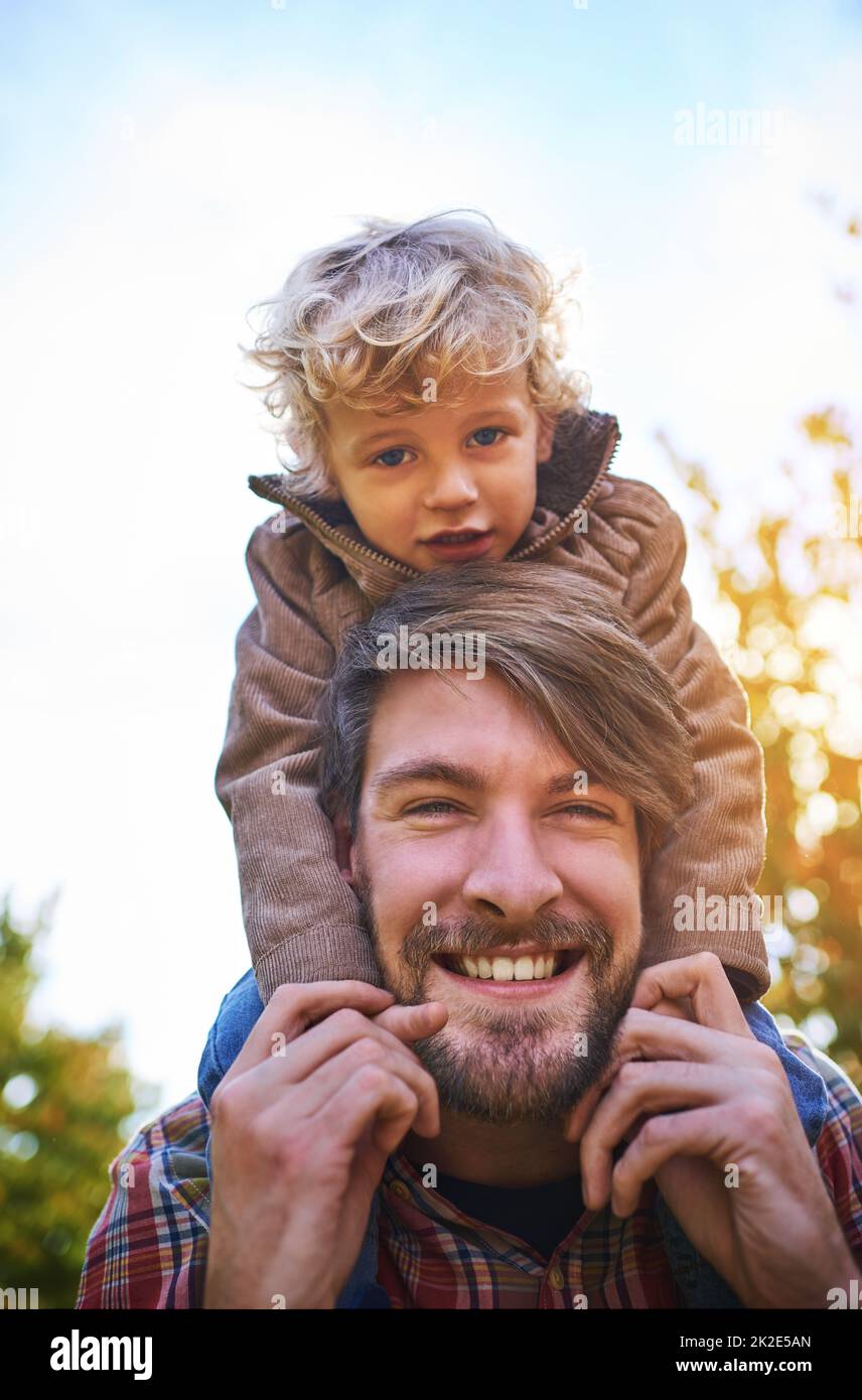 Bonding with his beautiful boy. Cropped portrait of a handsome young man piggybacking his son outside during autumn. Stock Photo