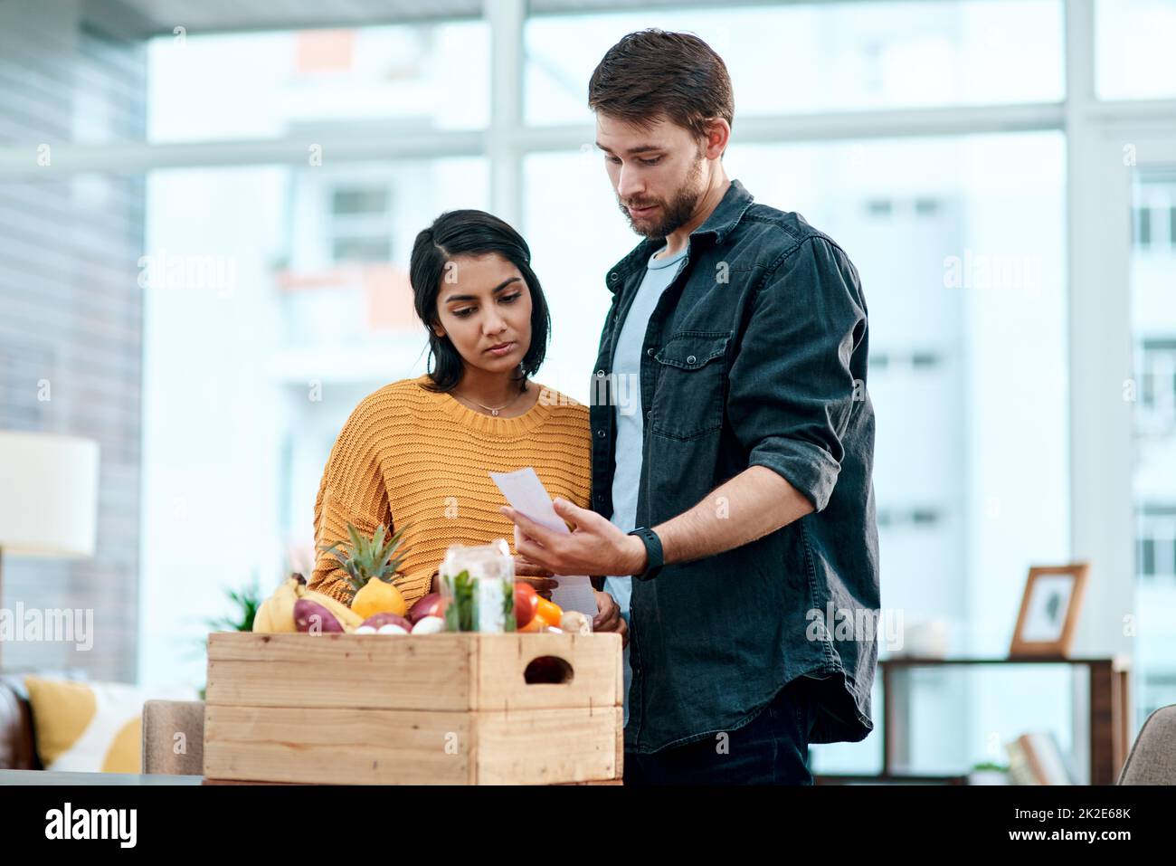 When keeping healthy comes at a cost. Shot of a young couple going through their receipts at home after buying groceries. Stock Photo