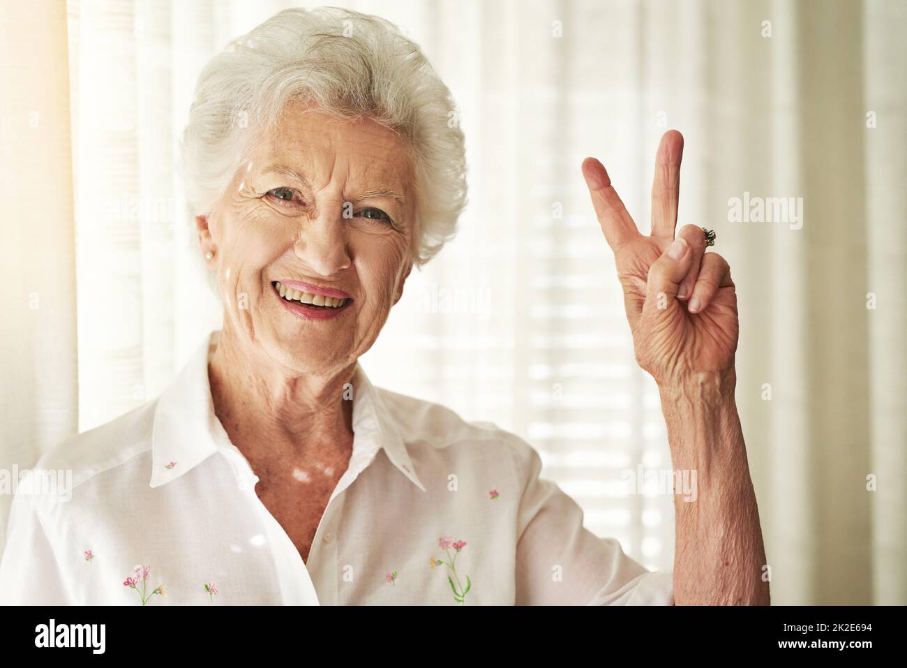 V for vitality. Portrait of a happy elderly woman showing a peace gesture at home. Stock Photo