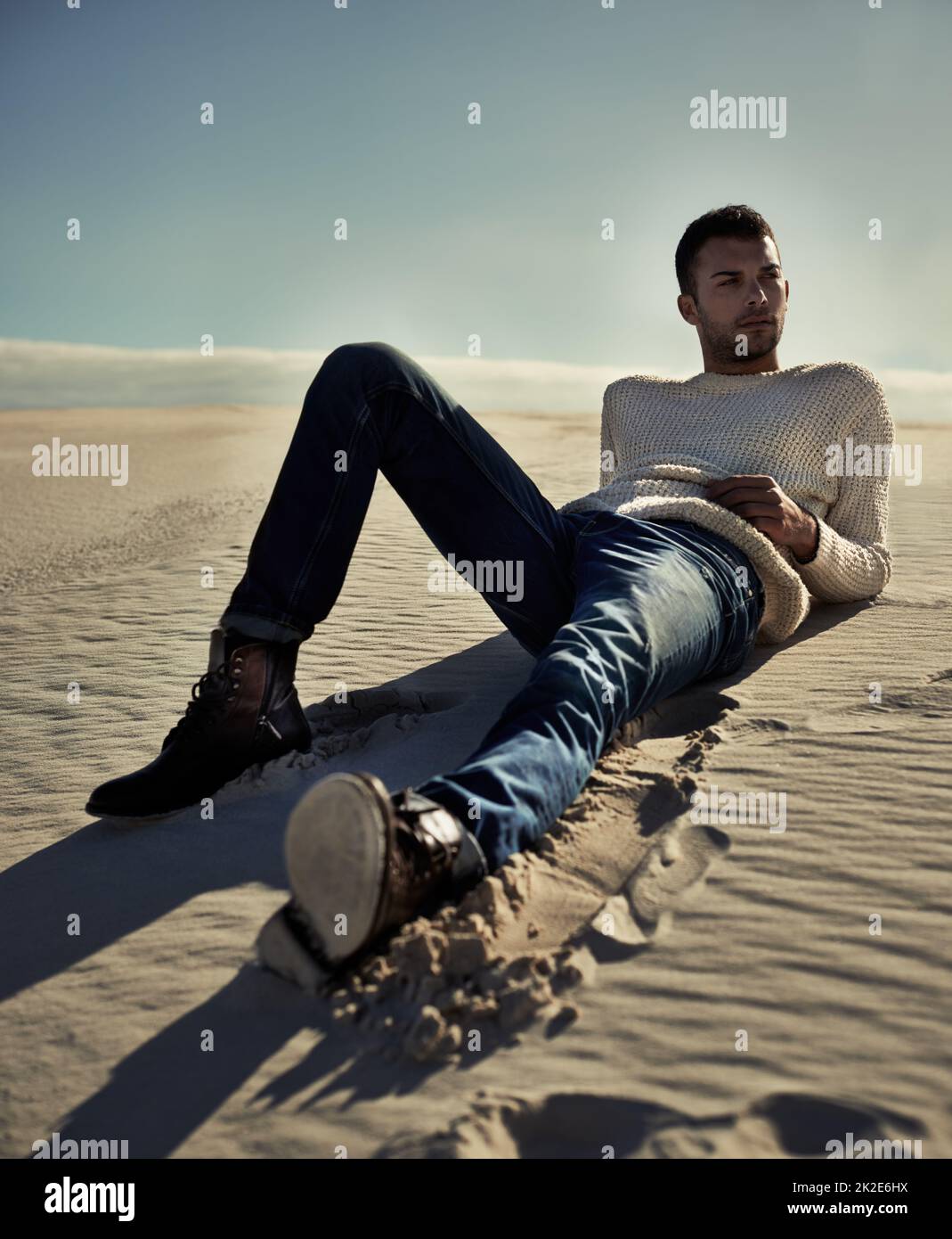 Stylish no matter where he is.... Full length of a handsome male model lying on the desert sand. Stock Photo