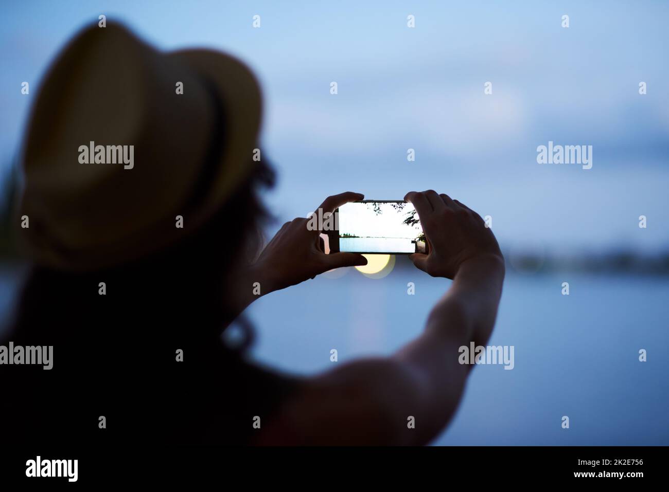Snapping pictures from dusk till dawn. Rearview shot of an unidentifiable young woman photographing a dusky landscape with her phone. Stock Photo
