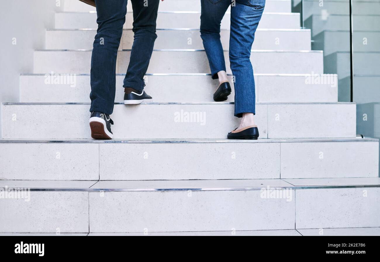 Reaching their goals together. Rearview shot of two unrecognisable businesspeople walking up a staircase together in an office. Stock Photo