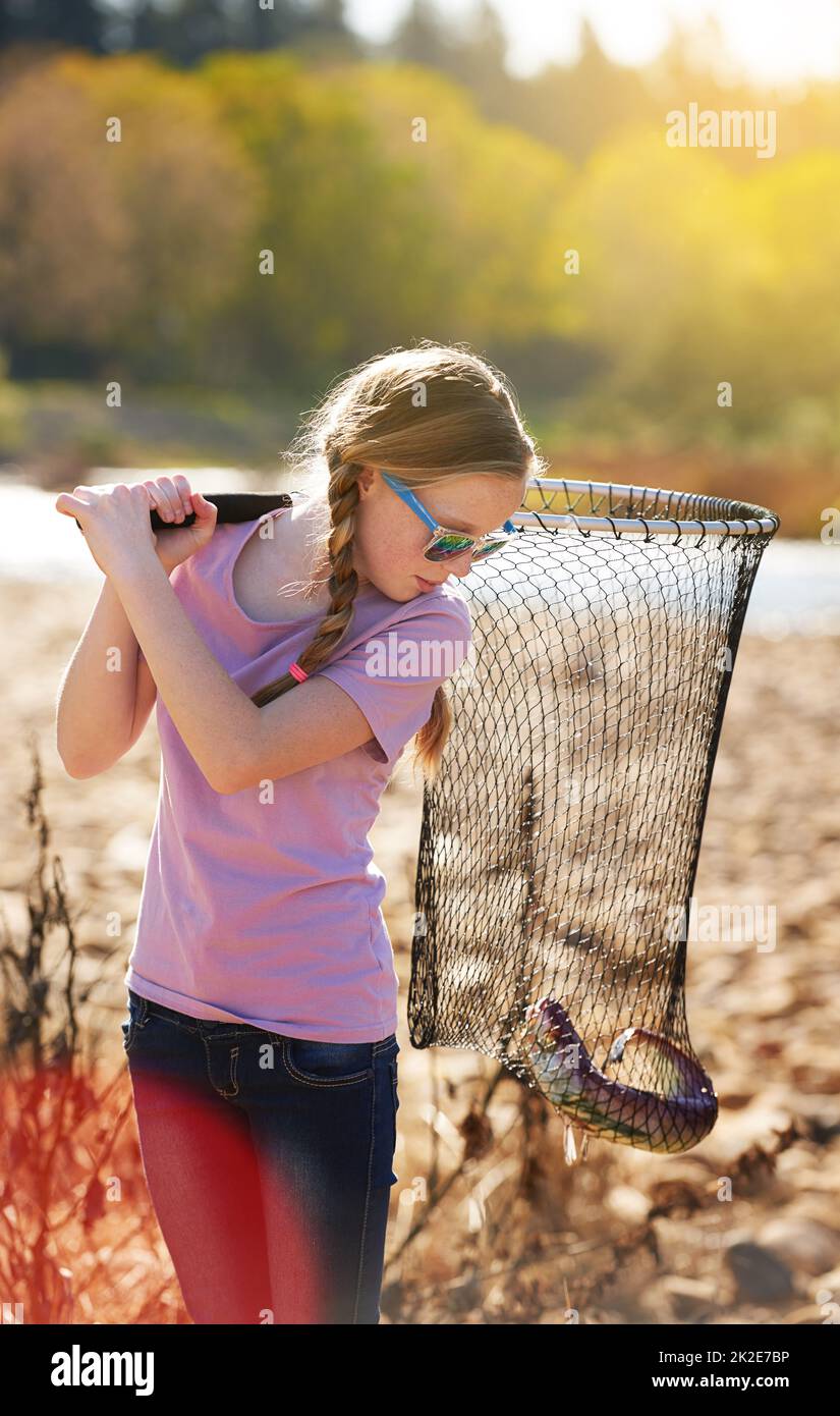 The one that didnt get away.... Shot of a young girl looking at the fish she caught with her net. Stock Photo