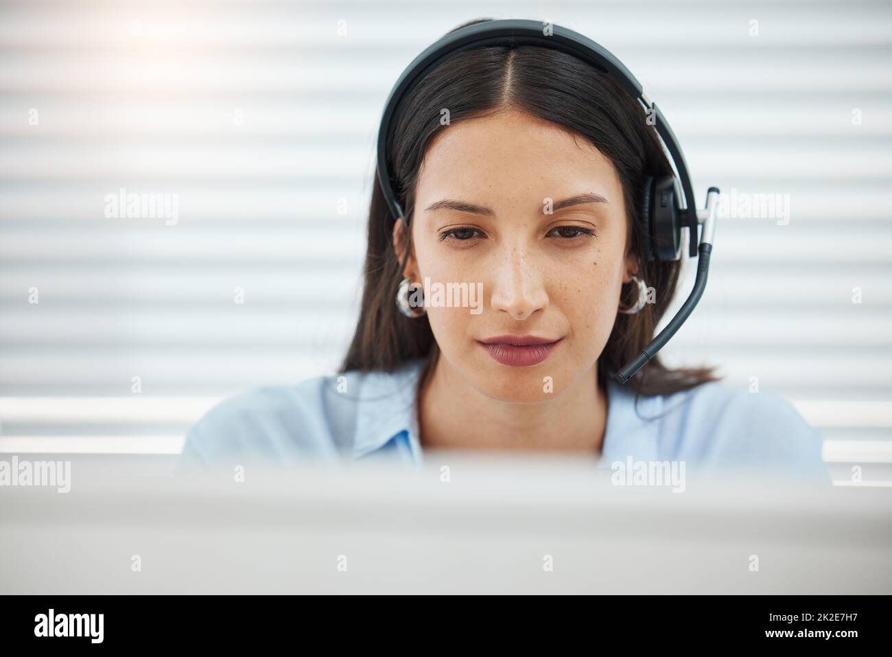 Challenges are always welcome. Shot of an attractive young saleswoman sitting alone in her office and wearing a headset. Stock Photo