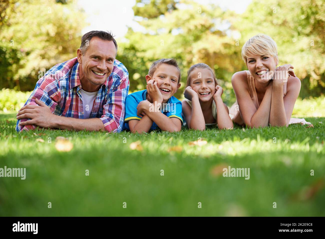These are the moments that count in life.... A front view portrait of a happy family lying on the grass outdoors. Stock Photo