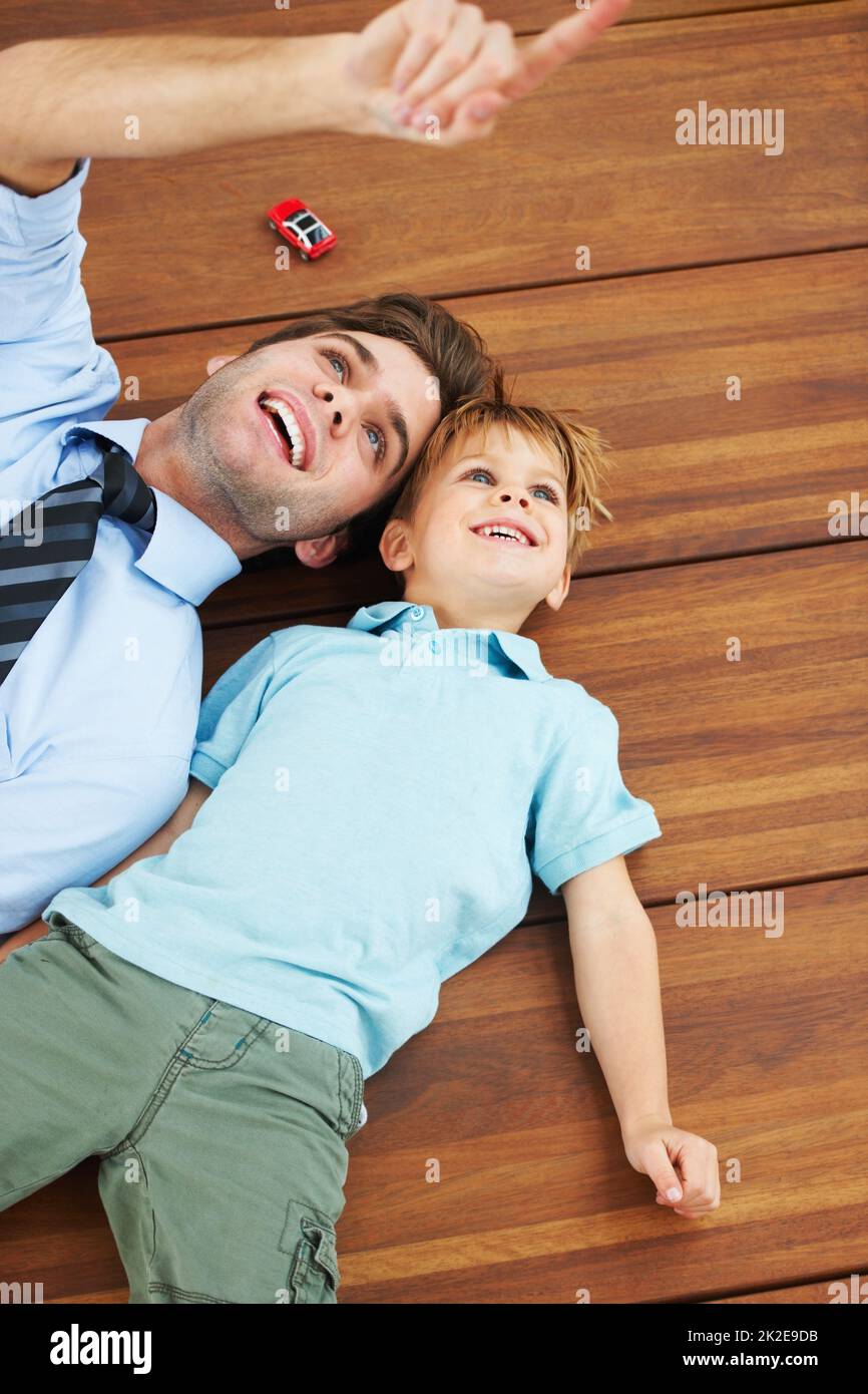 Look over there. A cute boy and his young father lying on the floor and looking up at something. Stock Photo