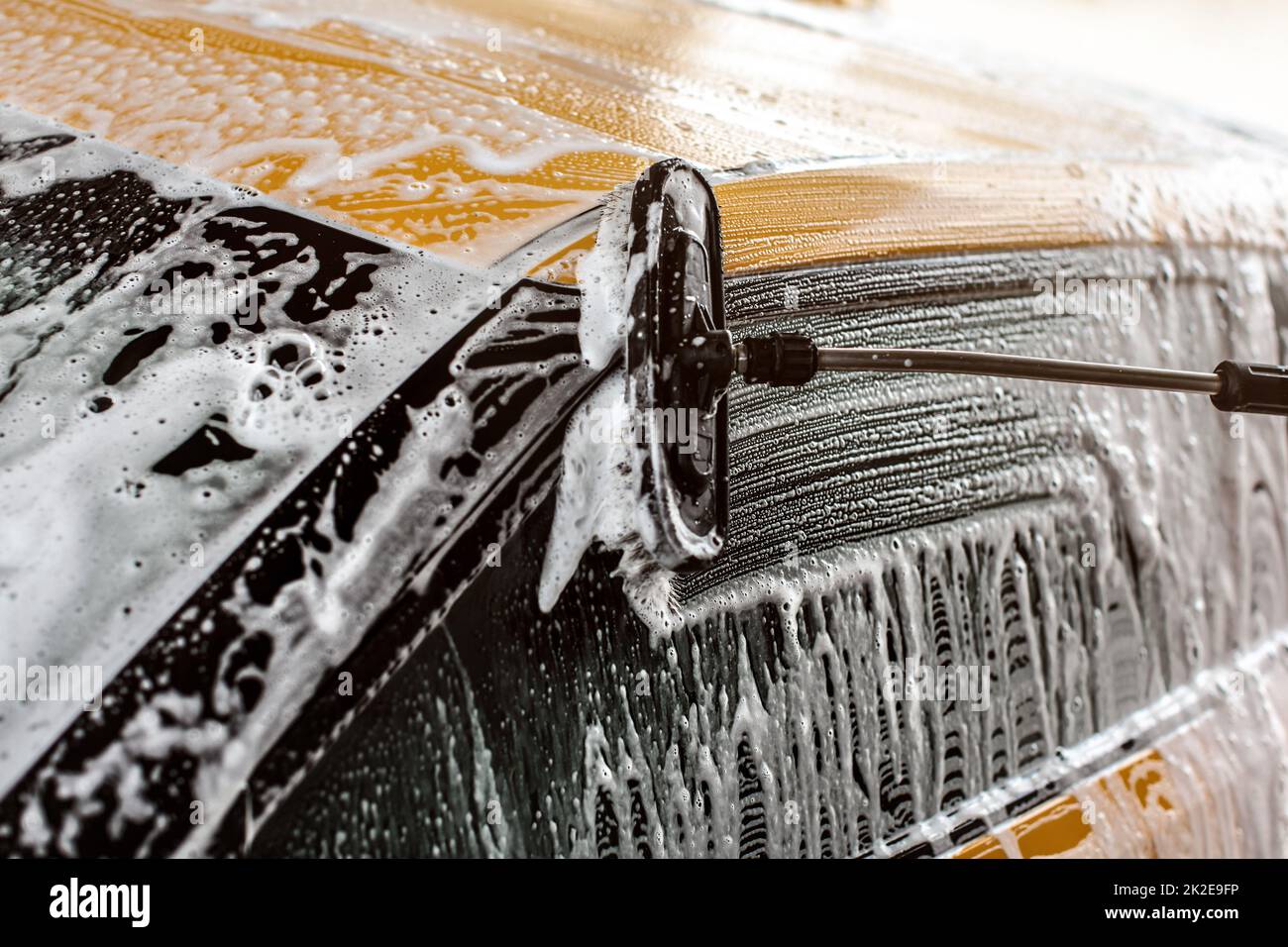 Side of yellow car being washed in self serve carwash, Brush leaving strokes on glass in shampoo and foam. Stock Photo