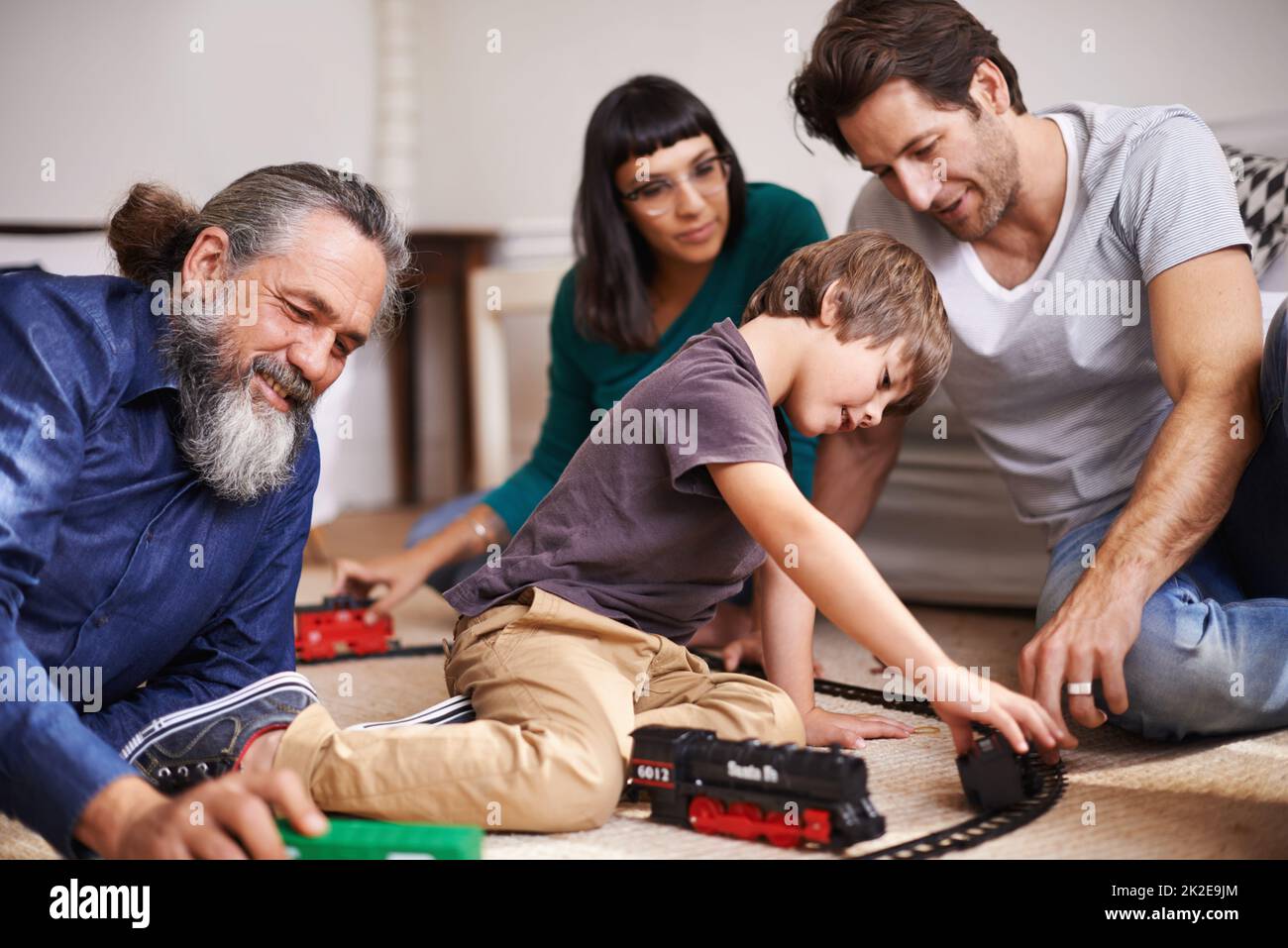 Family fun on the railroad. Cropped shot of a young child playing with a train set while his family watches. Stock Photo
