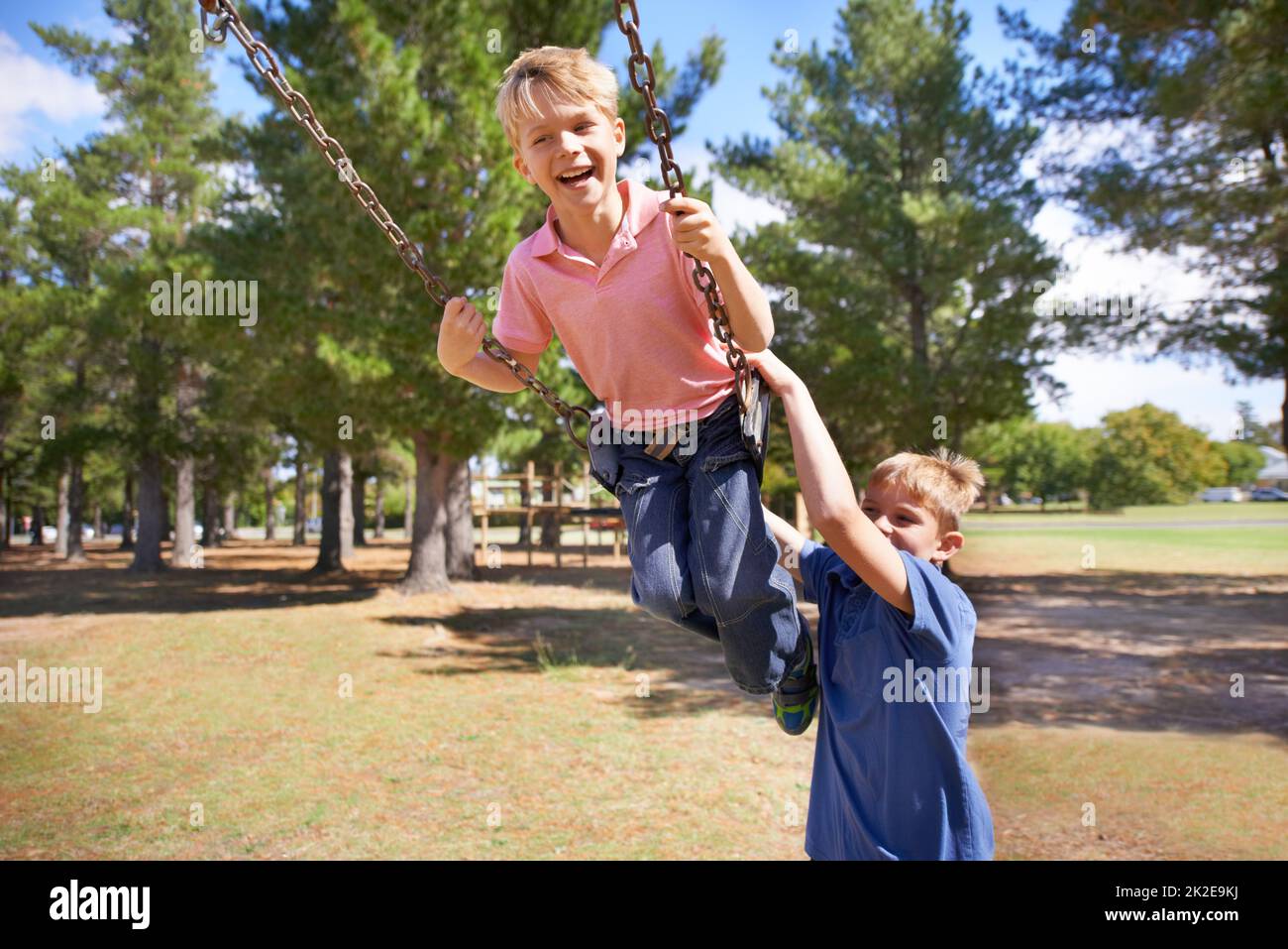 Higher and higher. A young boy enjoying the swings on the playground with friend. Stock Photo