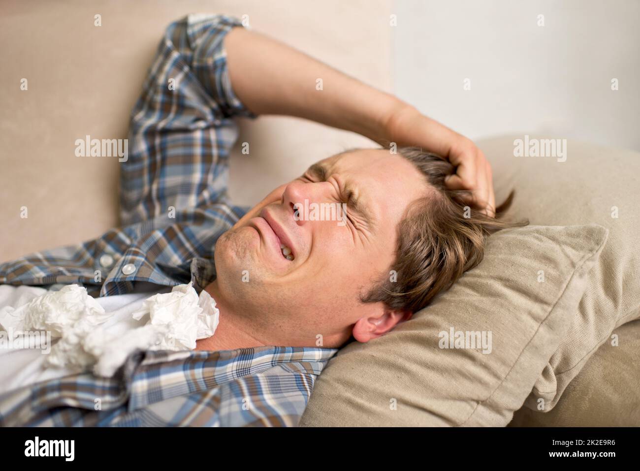 Dealing with a bad breakup. A young man crying while lying on the sofa with tissues. Stock Photo