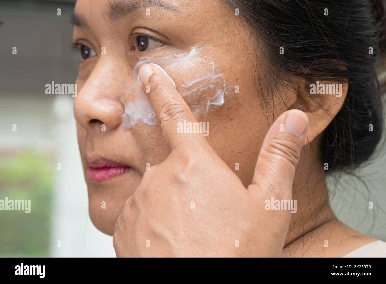 Asian lady woman applying cream skincare treatment to solve blemishes or melasma and dark spots in her face. Stock Photo
