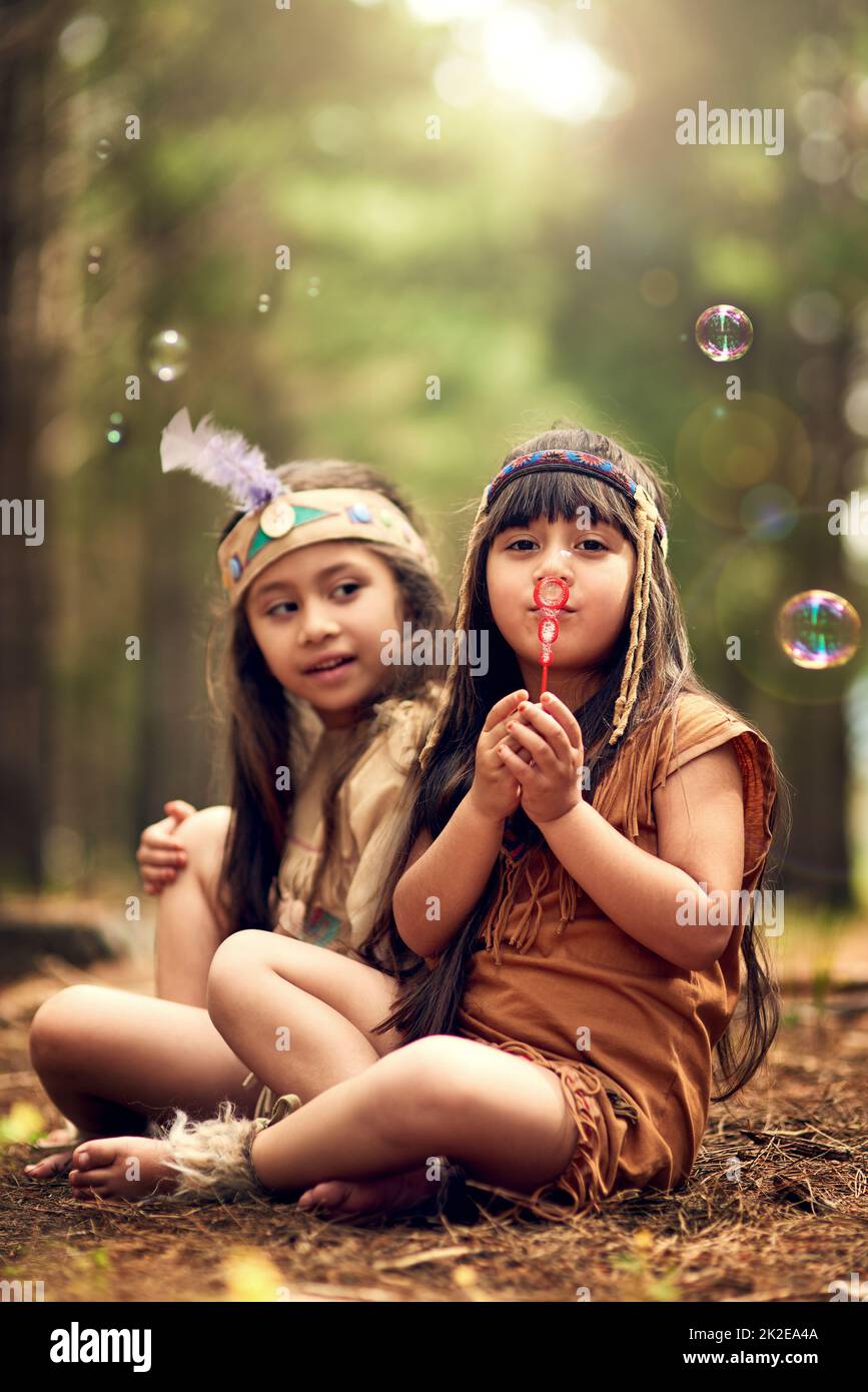 This is how we send smoke signals. Shot of two young kids blowing bubbles while playing dressup in the woods. Stock Photo