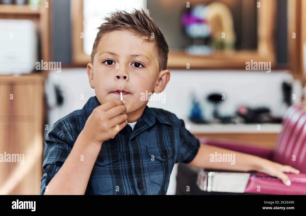 I got a sweet new hairstyle today. Portrait of an adorable little boy eating a lollipop after getting a fresh haircut at a salon. Stock Photo
