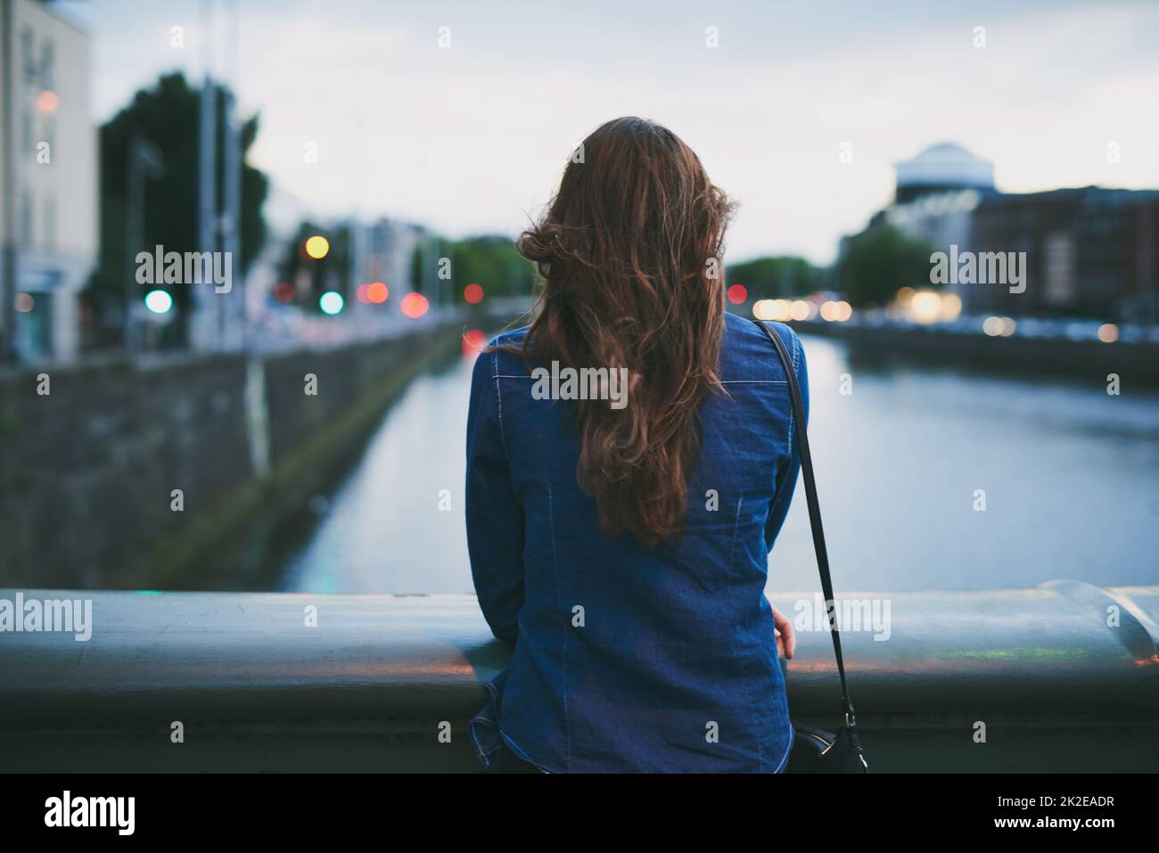 Taking in the sights. Rearview shot of an unrecognizable young woman taking in the city views while standing on a bridge. Stock Photo