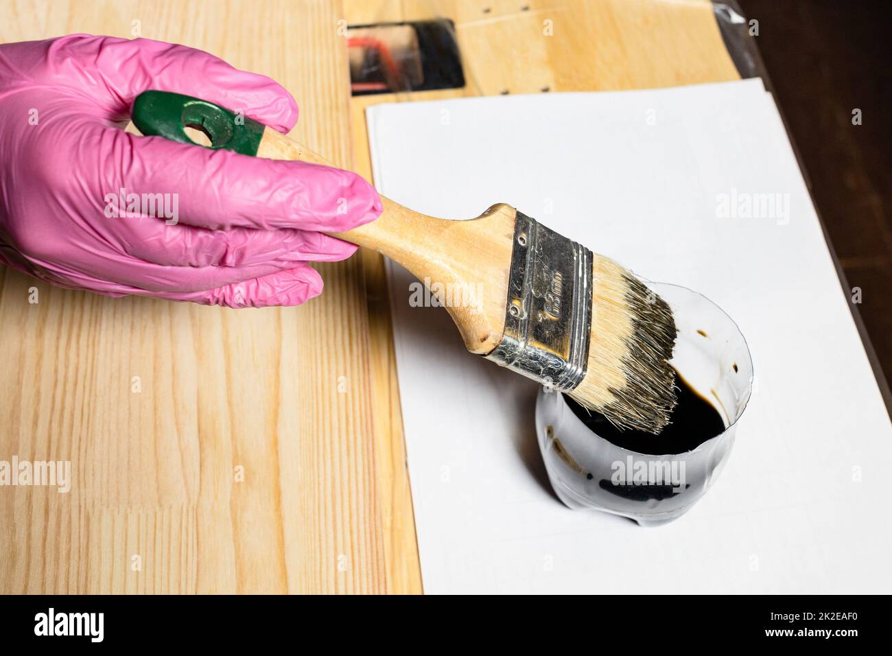 gloved hand dips brush into jar of wood stain Stock Photo