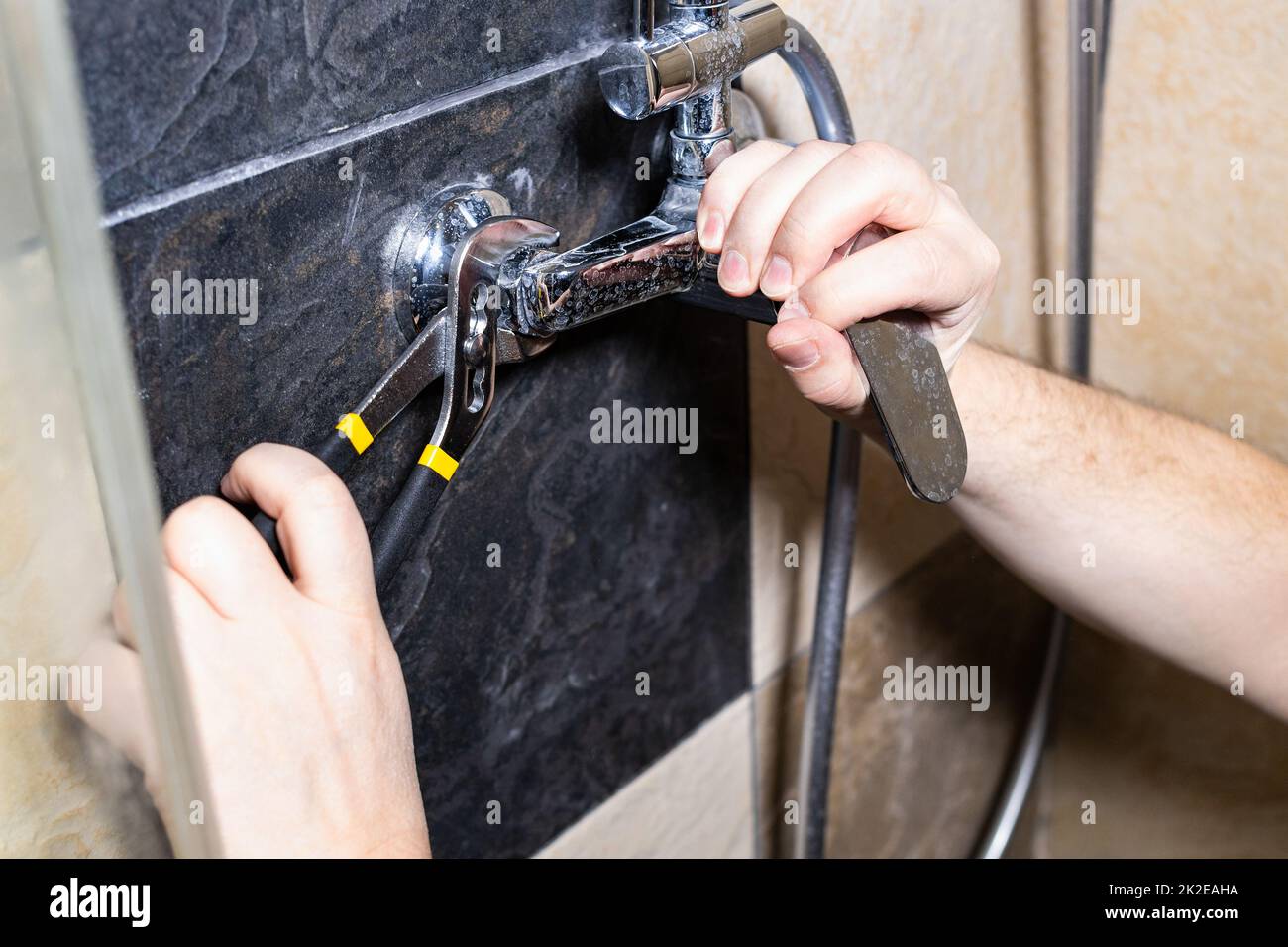 plumber installs shower faucet on tiled wall Stock Photo