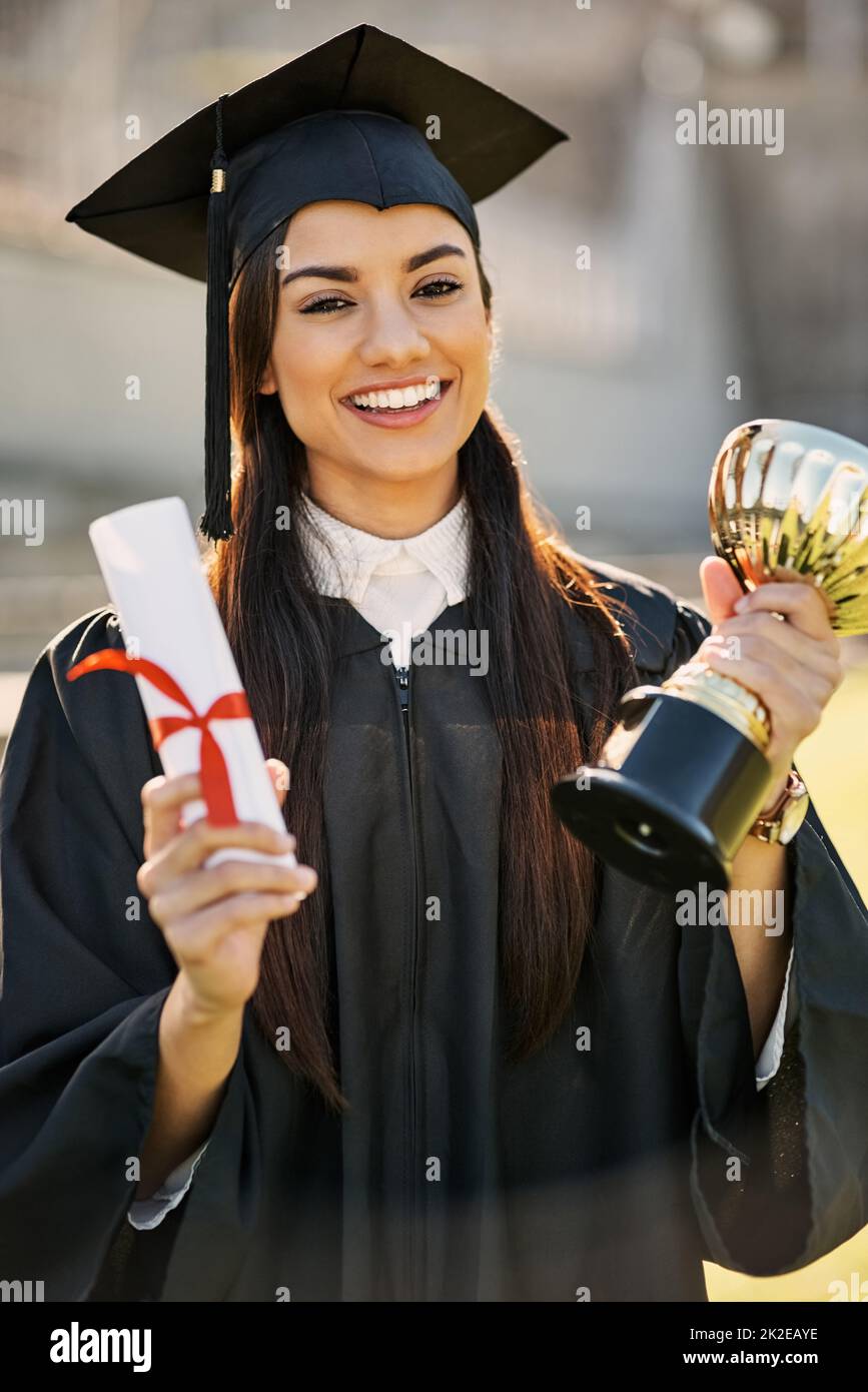 Shes achieved outstanding merit. Portrait of a student holding her diploma and trophy on graduation day. Stock Photo
