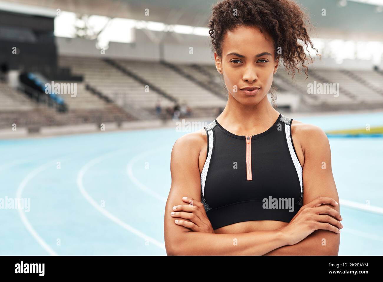 Staying focused on my end goal. Cropped portrait of an attractive young athlete standing alone with her arms folded before running a track field. Stock Photo