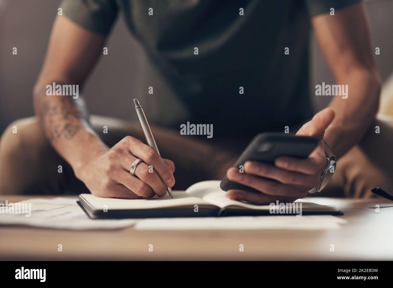 The best personal finance app on the market. Shot of an unrecognisable man using a smartphone while going through paperwork at home. Stock Photo