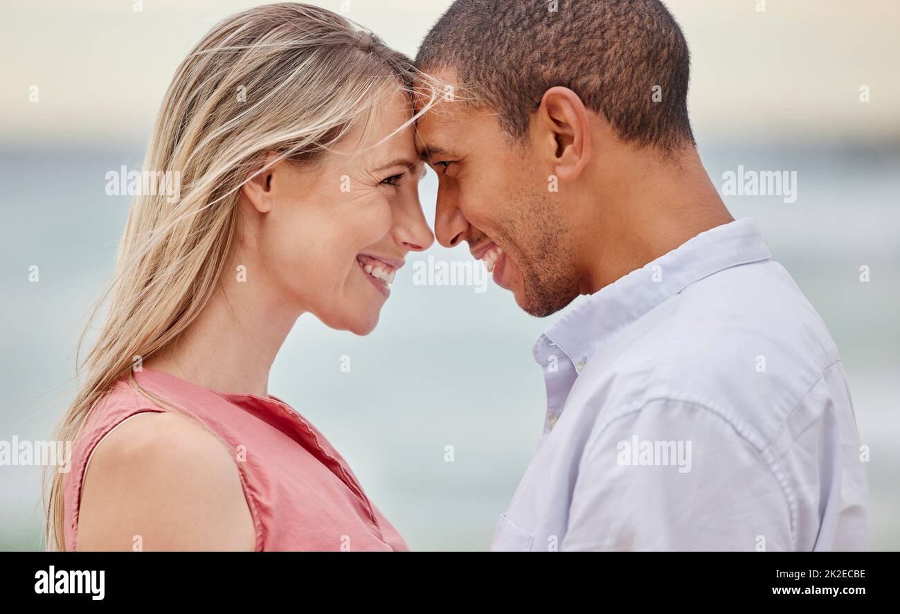 Portrait of couple at the beach with their forehead touching. Multiracial man and woman in relationship, happy, smiling and in love on vacation Stock Photo
