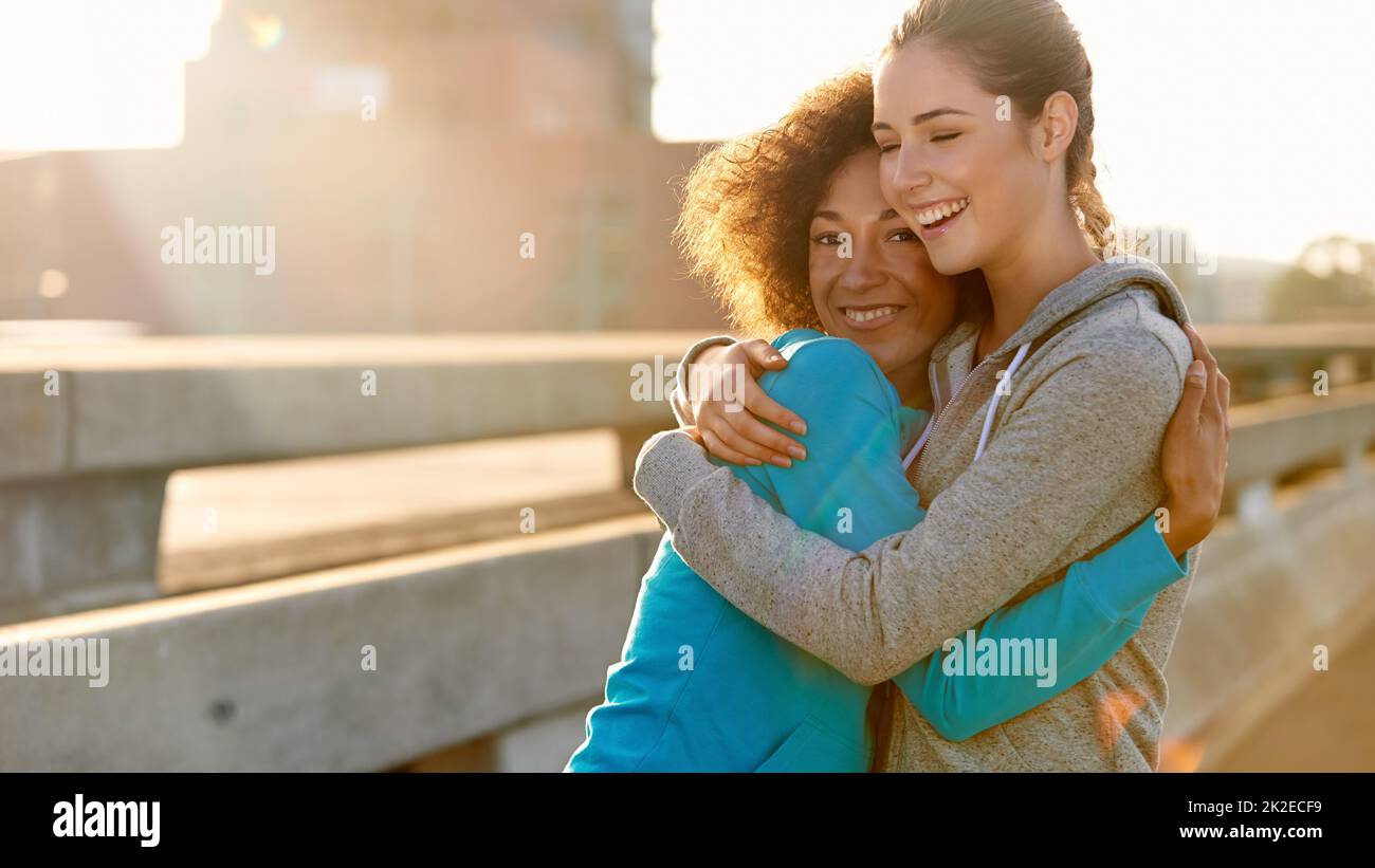Even jogging is awesome when we do it together. Portrait of two female joggers hugging each other and laughing before a run through the city. Stock Photo