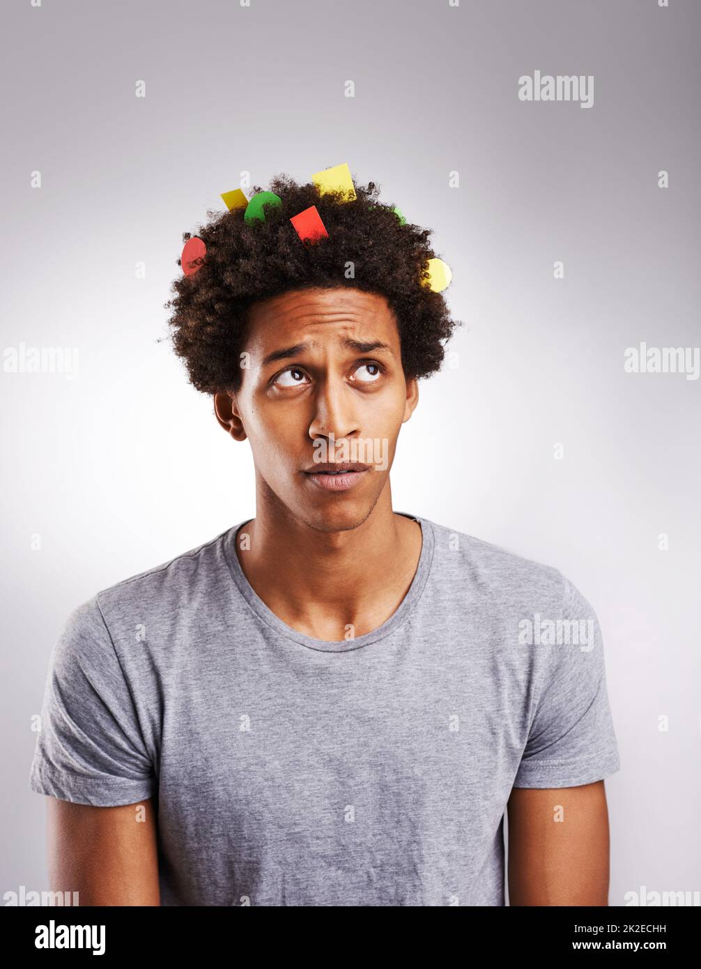 Its time to think in color. Shot of a young man with colorful paper in his hair against a gray background. Stock Photo
