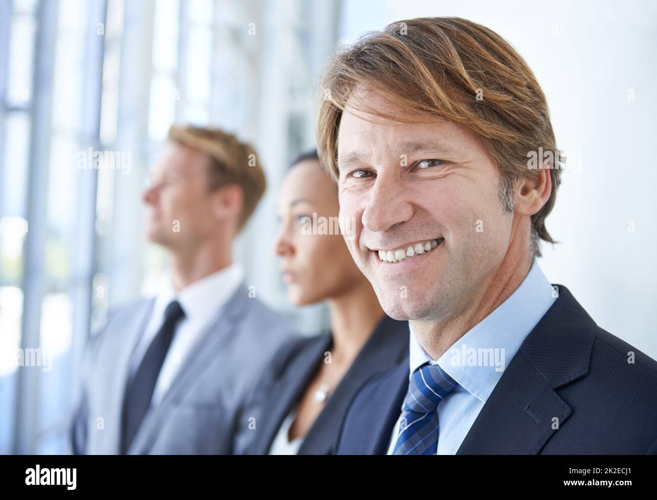 One day Ill be on Fortune 500s top 50. A smiling businessman with two coworkers behind him. Stock Photo