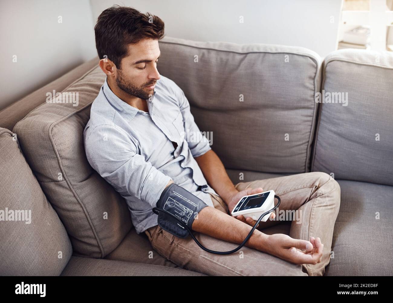 Doing my regular checkup. Shot of a young man taking his own blood pressure readings with a blood pressure monitor at home. Stock Photo