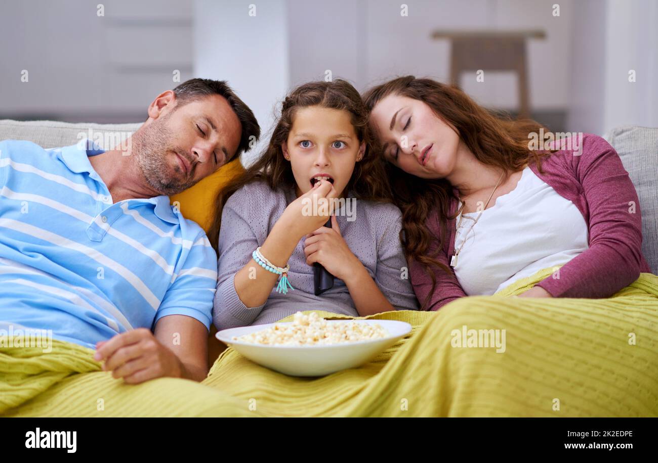 Movie night ran too long for her parents. Cropped shot of a young girl watching a movie while both her parents sleep on either side of her. Stock Photo