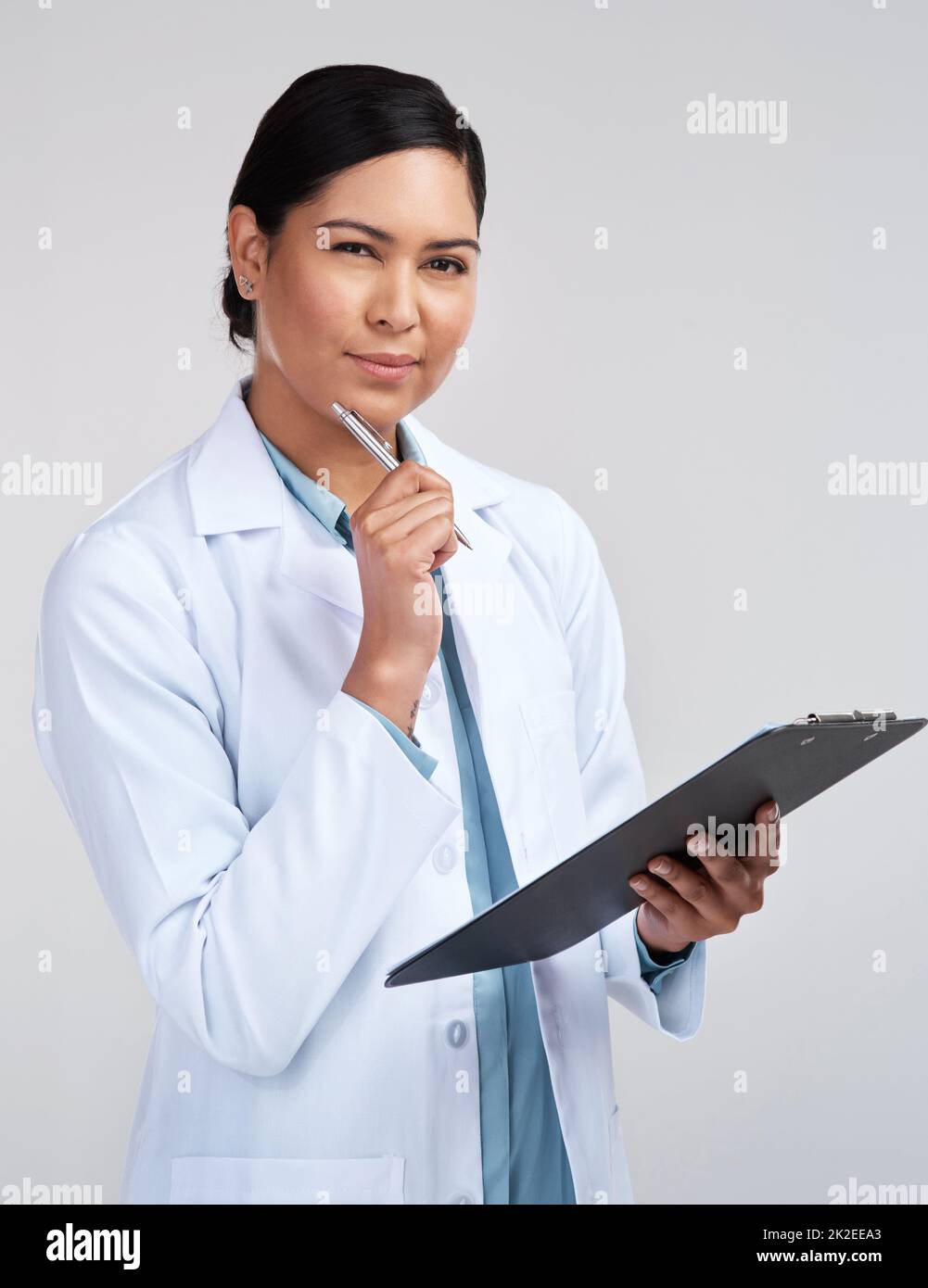 This requires a little thought. Cropped portrait of an attractive young female scientist looking thoughtful while working on a clipboard in studio against a grey background. Stock Photo