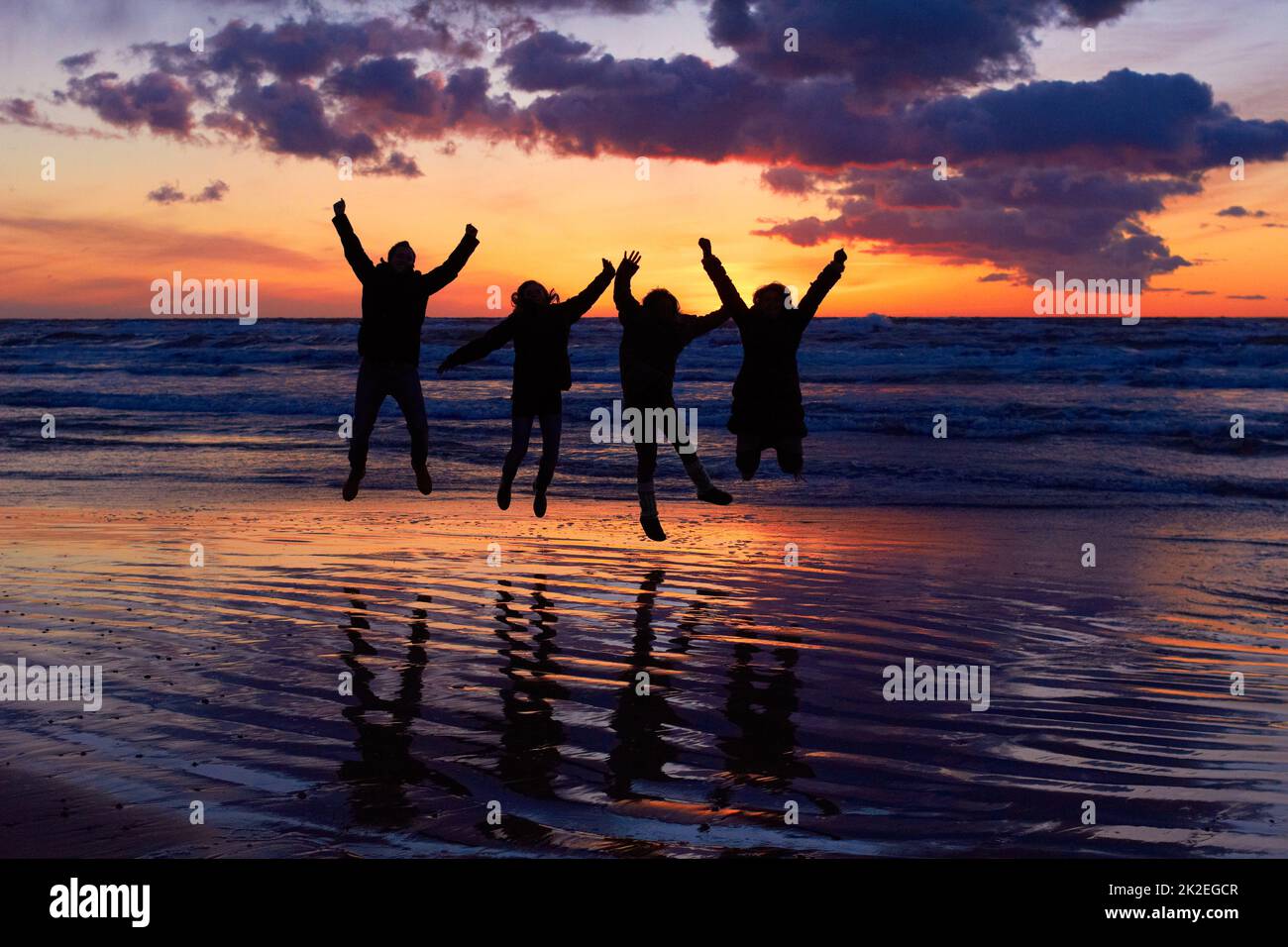 Loving the vitality of nature. Silhouette of a group of people jumping on the beach at sunset. Stock Photo