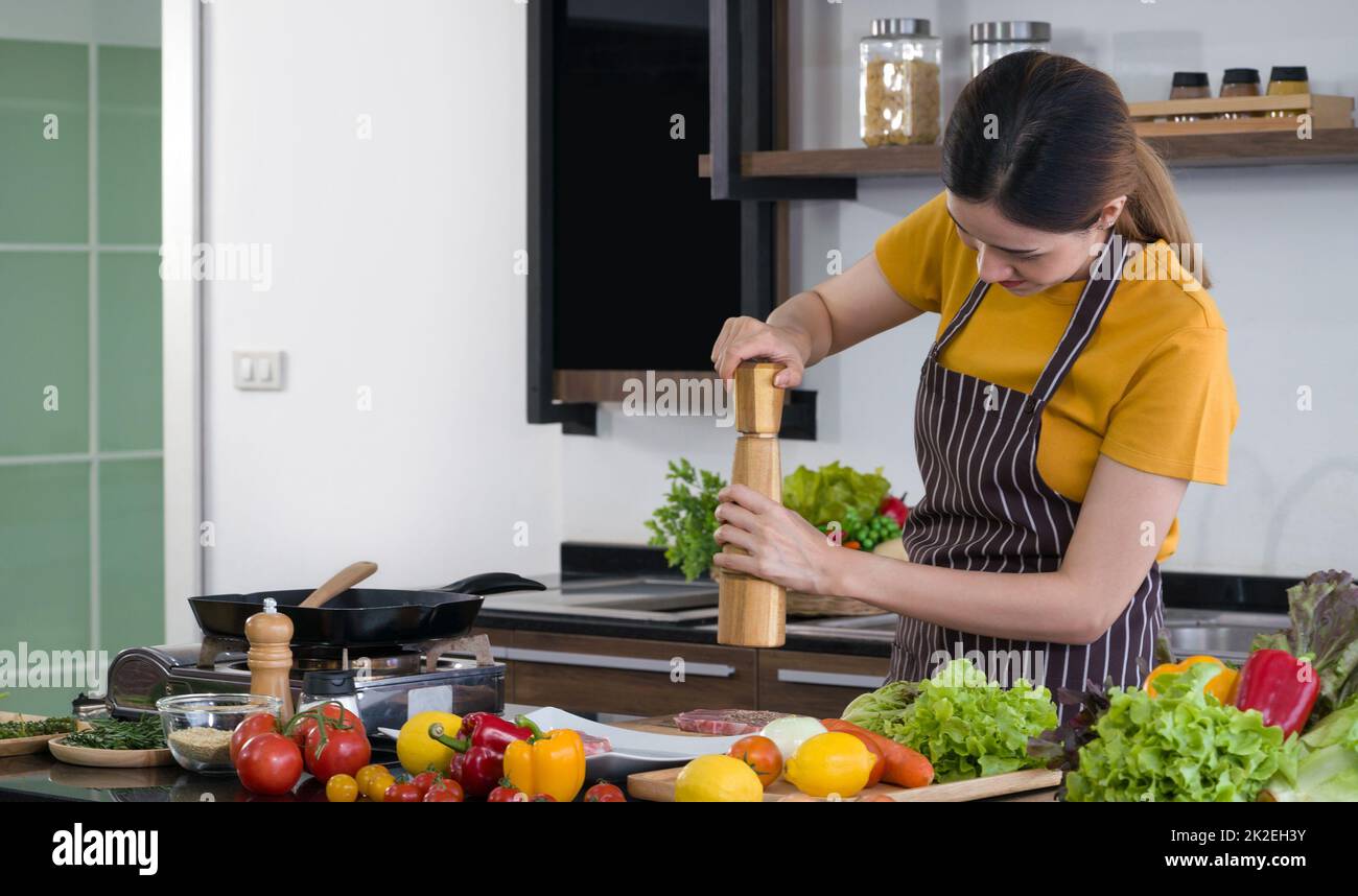Young housewife putting pepper on the pork before cooking it in to a