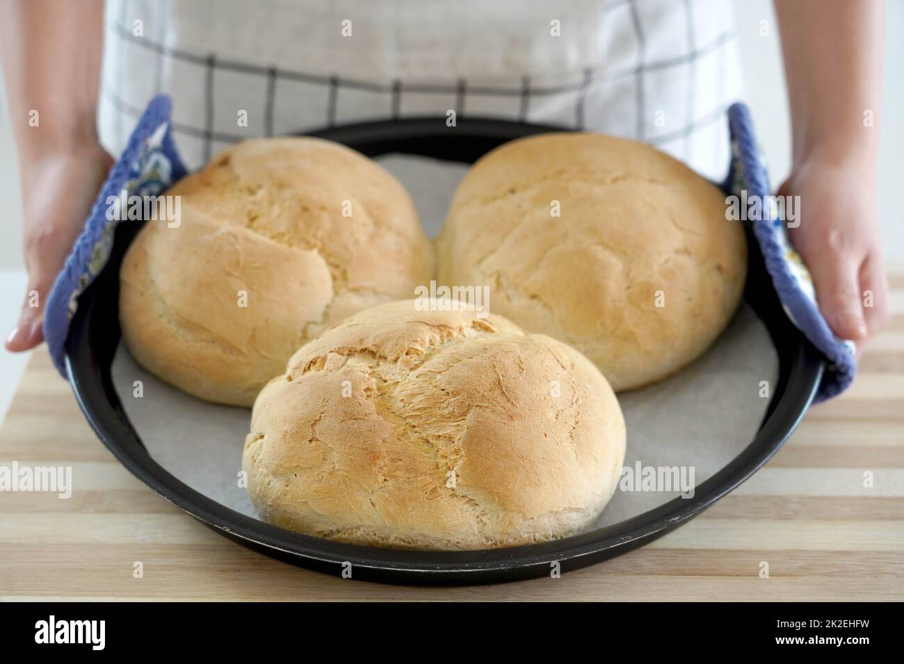 Woman showing three homemade loaves of bread in baking tray freshly baked Stock Photo