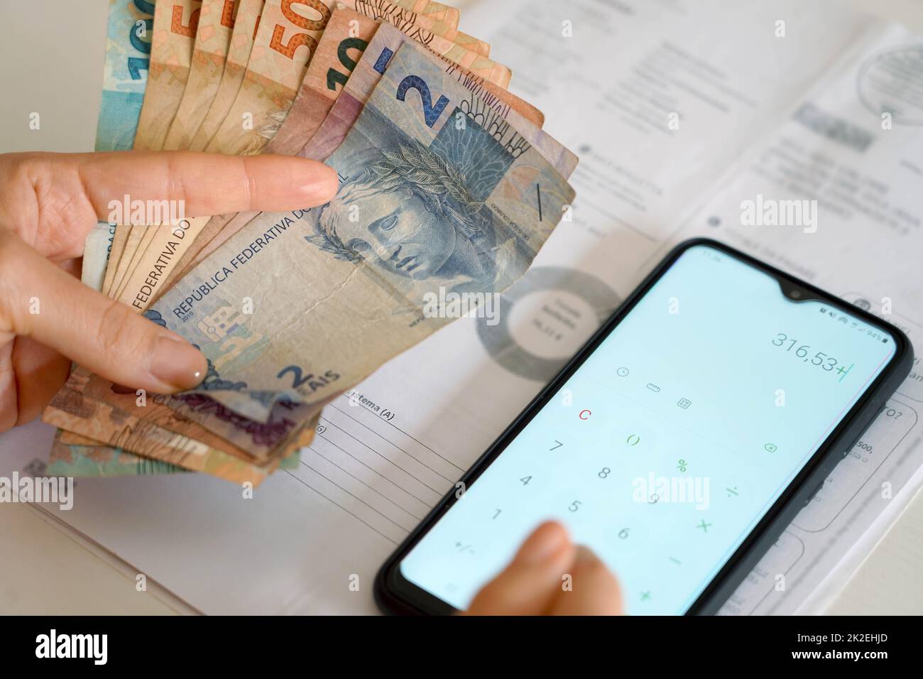 Rising prices of energy bills during financial crisis. Woman holding Real banknotes of Brazil counting expenses electricity bill or gas bill on calculator. Stock Photo