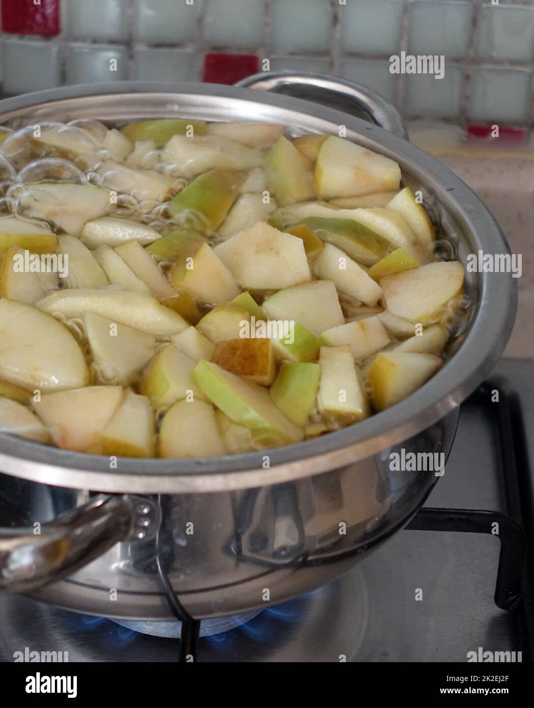 freshly chopped green sour apple pieces boiling in pot,make homemade apple juice Stock Photo