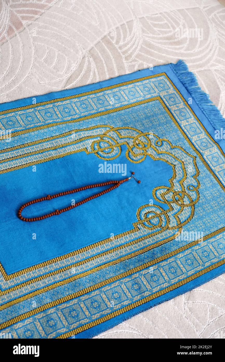 A blue, prayer rug, in the house, of a Muslim, his rosary, next to it, a prayer, rug, for