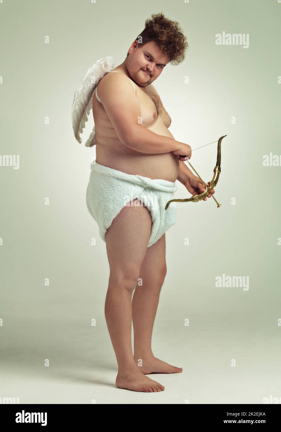 Shooting straight. An obese man dressed as a cherub with a bow and arrow. Stock Photo
