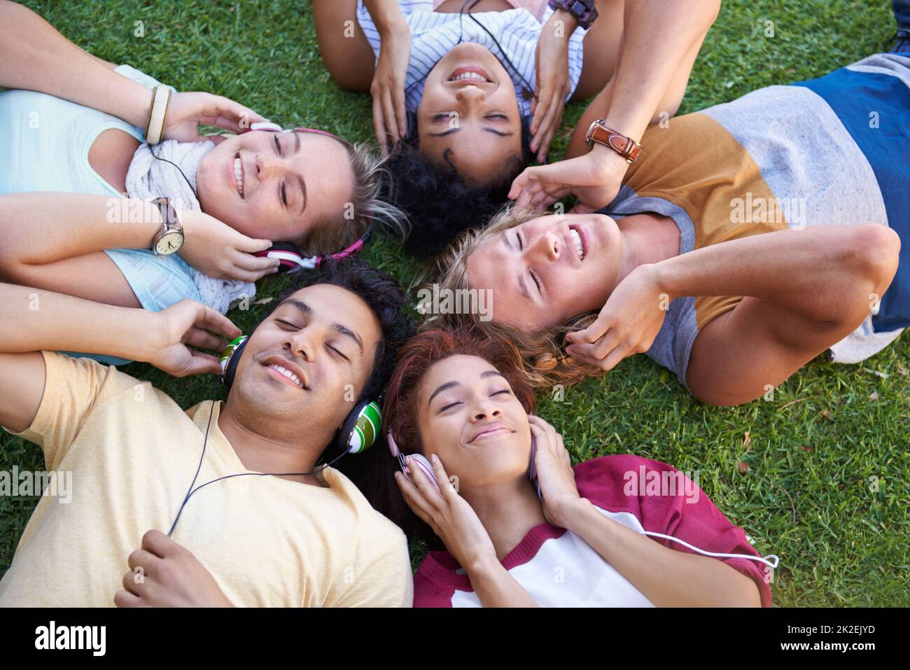 We all love music. High angle of a group of friends lying on their backs on the grass in a park and listening to music. Stock Photo