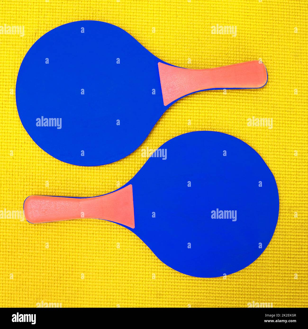 It takes two to tango. High angle shot of two blue table tennis rackets placed on top of a yellow background inside of a studio. Stock Photo