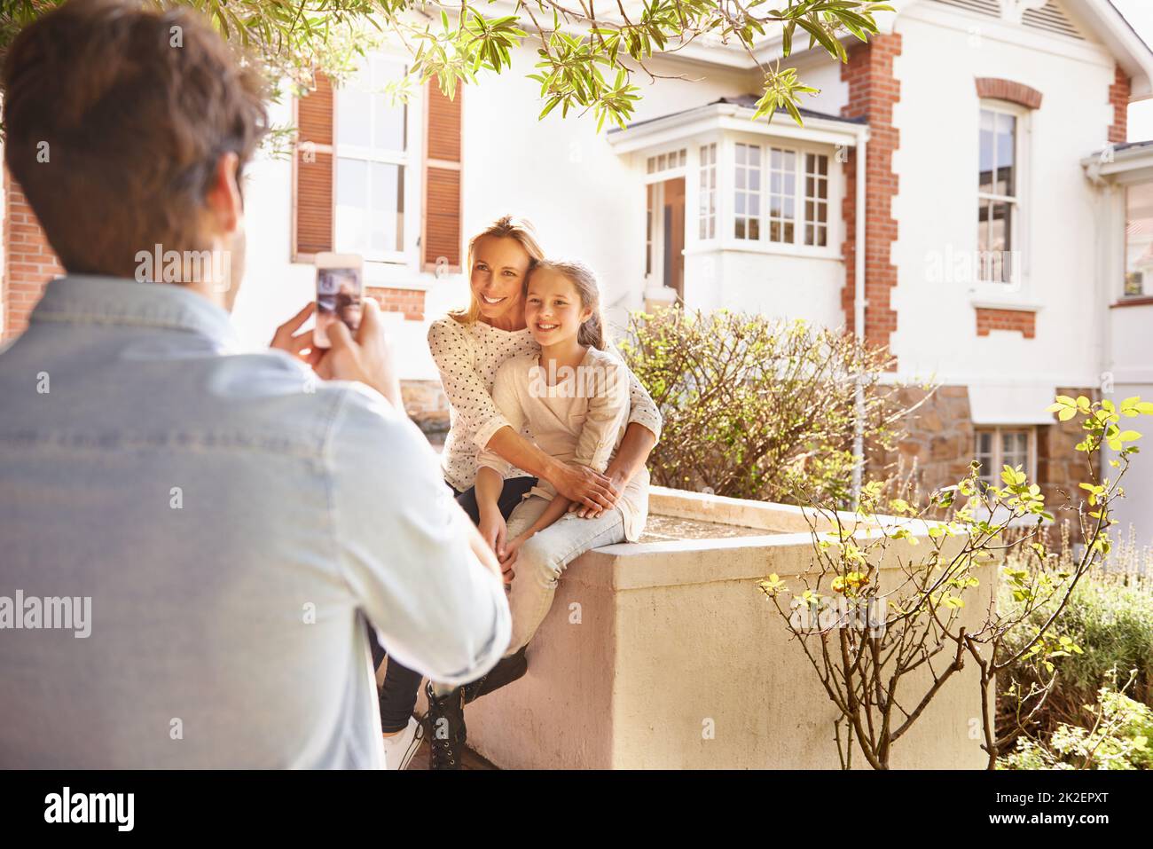 Smile. A man taking a photo of his wife and daughter in their garden. Stock Photo
