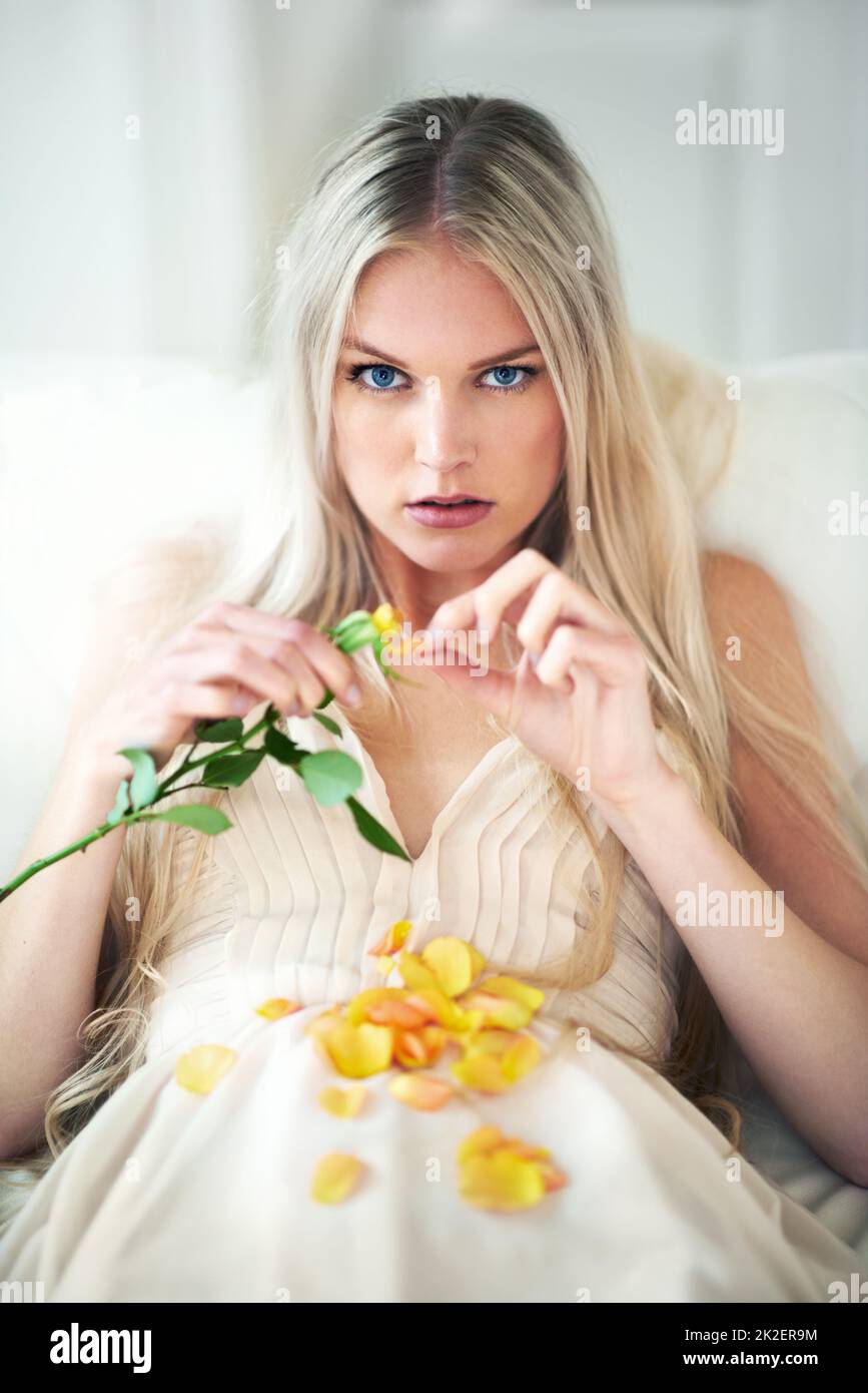 He loves me.... Portrait of an attractive woman pulling petals from a rose on her bed. Stock Photo