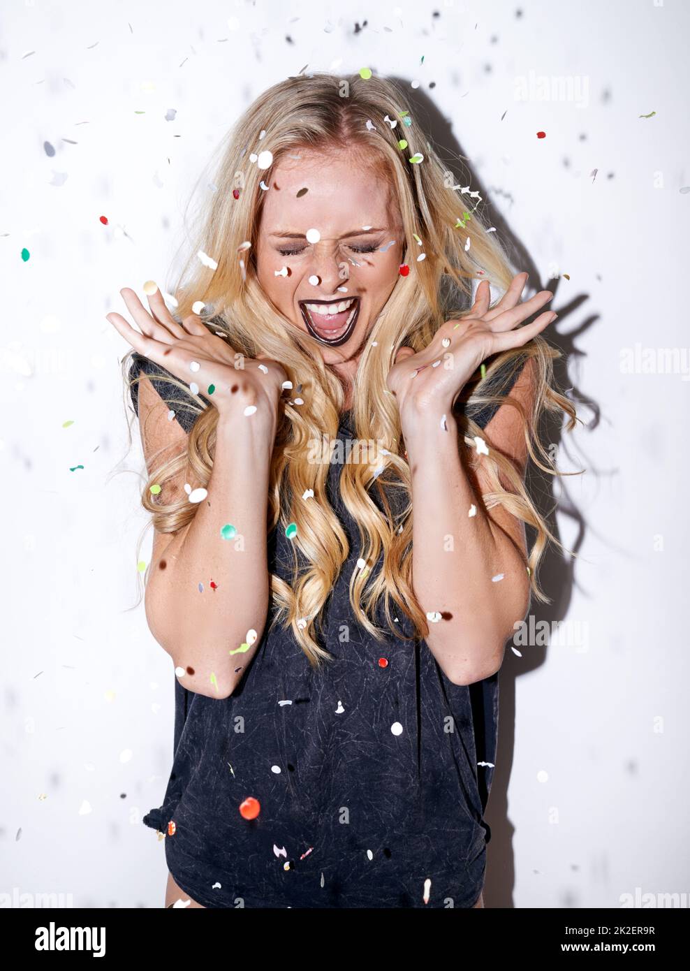 Lets get the party started. Shot of an attractive young woman shouting in excitement as confetti falls down on her. Stock Photo