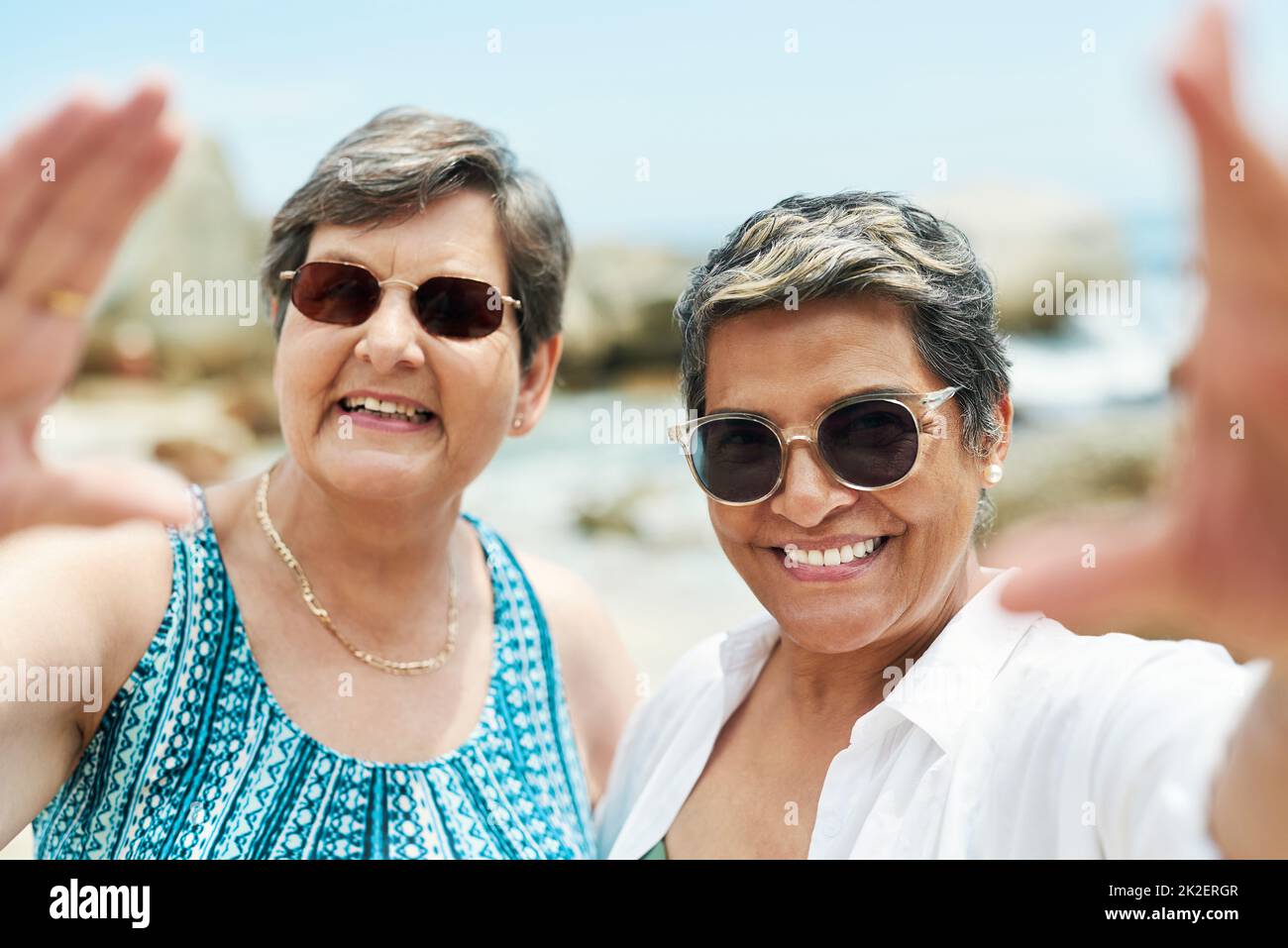 How can we not a selfie on the beach. Shot of two mature friends standing together and posing for a selfie during a day out on the beach. Stock Photo