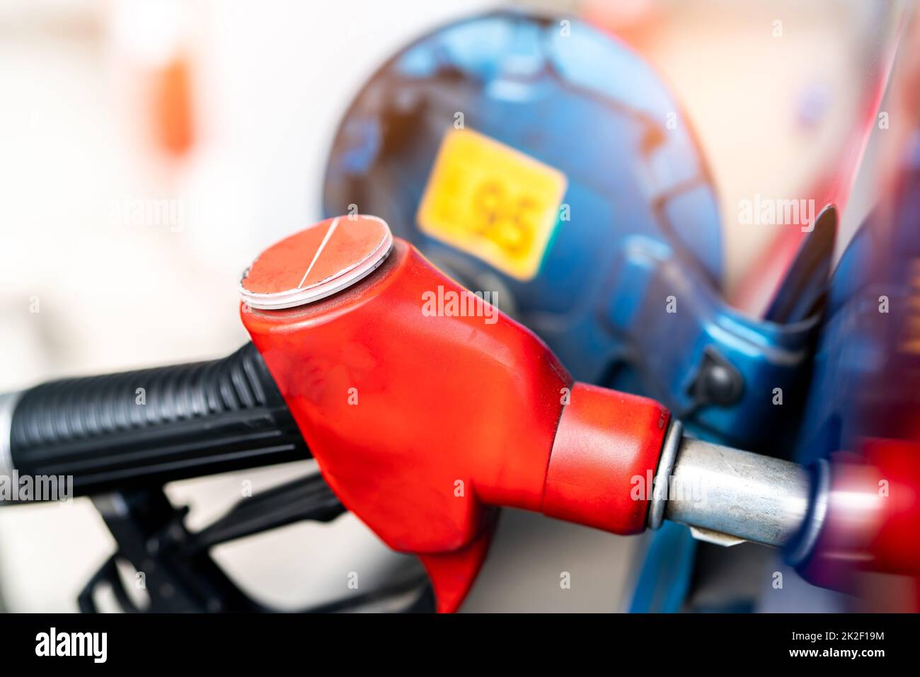 Close-up red fuel nozzle. Gasoline pump nozzle. Car fueling at gas station. Refuel fill up with petrol gasoline. Petrol pump filling fuel nozzle in fuel tank of car at gas station. Oil price crisis. Stock Photo
