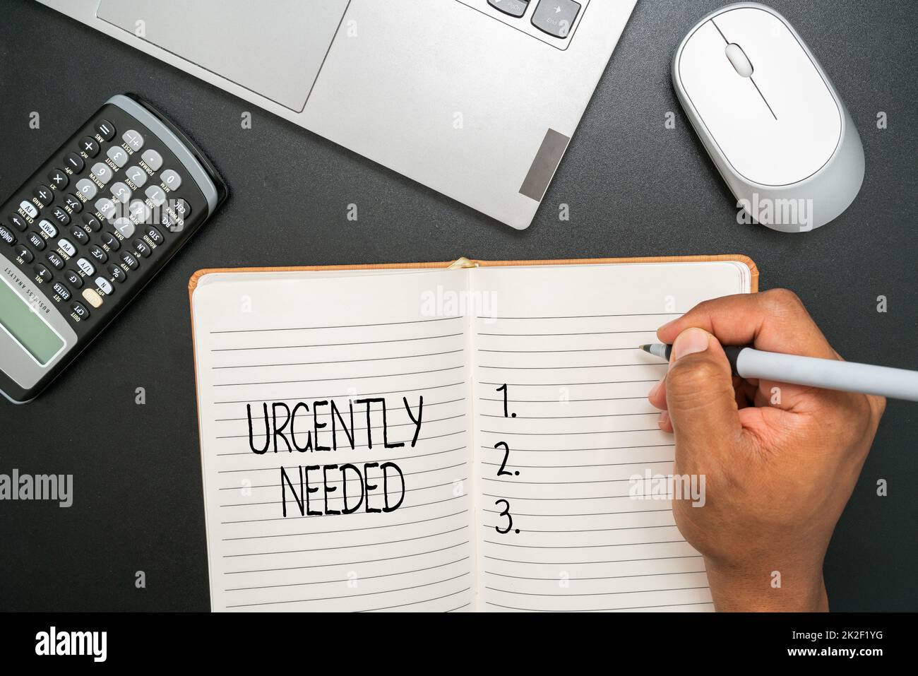 Hand writing sign Urgently Needed. Business concept Urgently Needed Office Supplies Over Desk With Keyboard And Glasses And Coffee Cup For Working Stock Photo