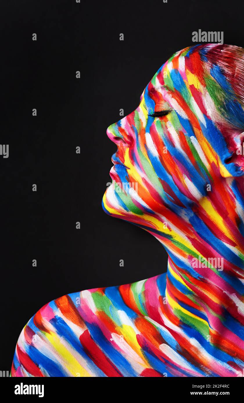 Theres no beauty without color. Studio shot of a young woman posing with brightly colored paint on her face against a black background. Stock Photo
