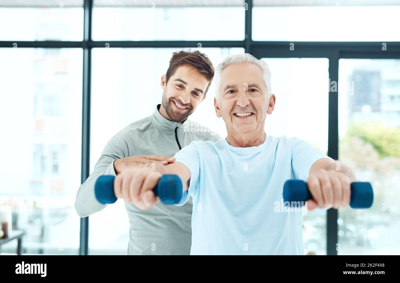 Hes putting in the effort for a healthier life. Shot of a friendly physiotherapist helping his senior patient work out with weights. Stock Photo