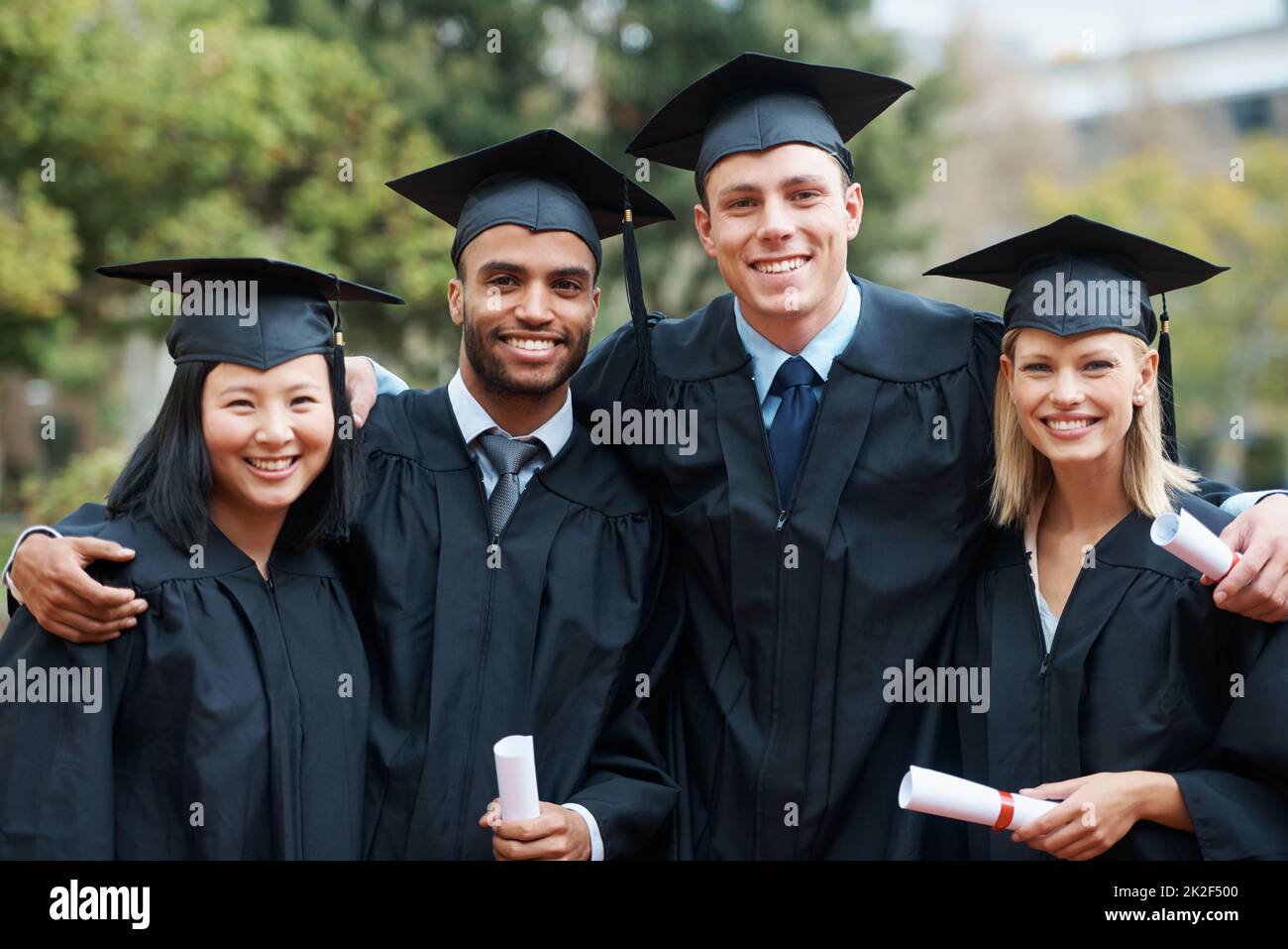 Students and fellow graduates. A group of college graduates standing in cap and gown and holding their diplomas. Stock Photo