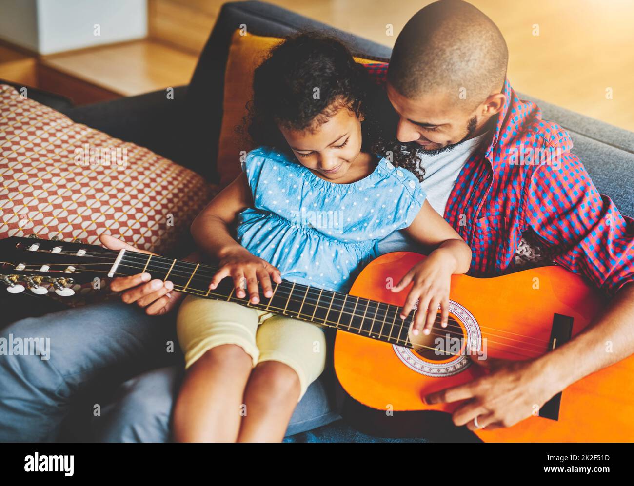 To share music is to share love. Shot of an adorable little girl and her father playing a guitar together on the sofa at home. Stock Photo