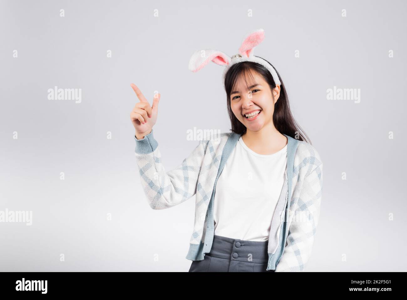Smiling happy woman wearing rabbit ears pointing finger something out space away side Stock Photo